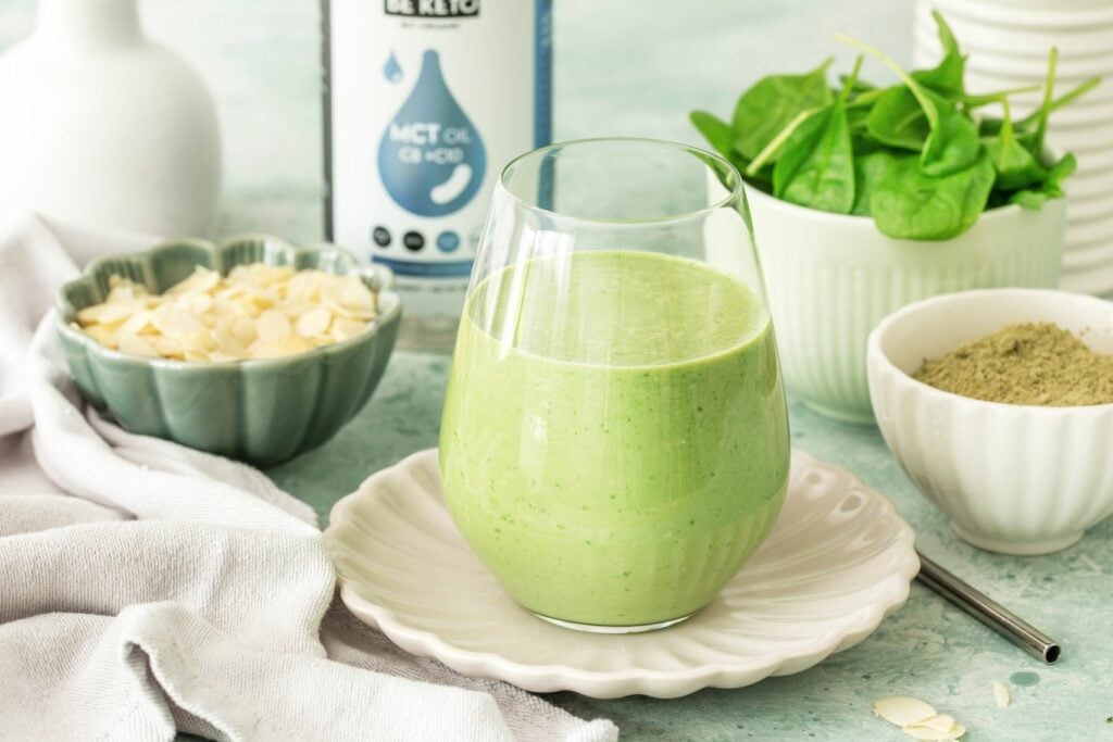 Grüner Keto Smoothie im Glas, daneben Spinat, Matcha, Mandelblättchen und BeKeto MCT-Öl C8 + C10