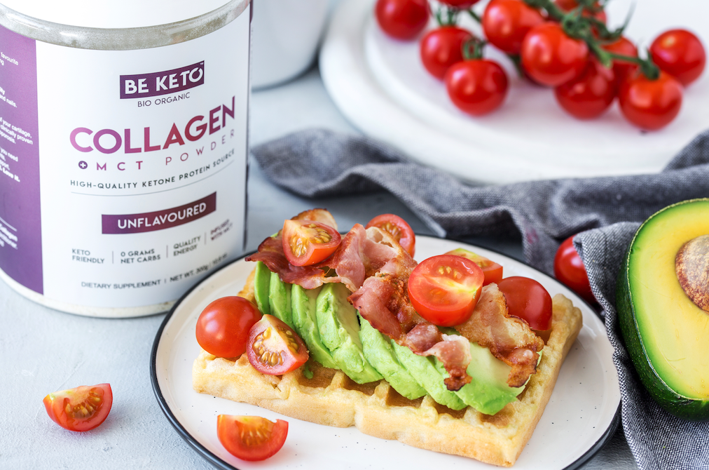 Keto Käsewaffel mit Avocado, Speck und Kirschtomaten auf einem Teller, daneben BeKeto Collagen + MCT