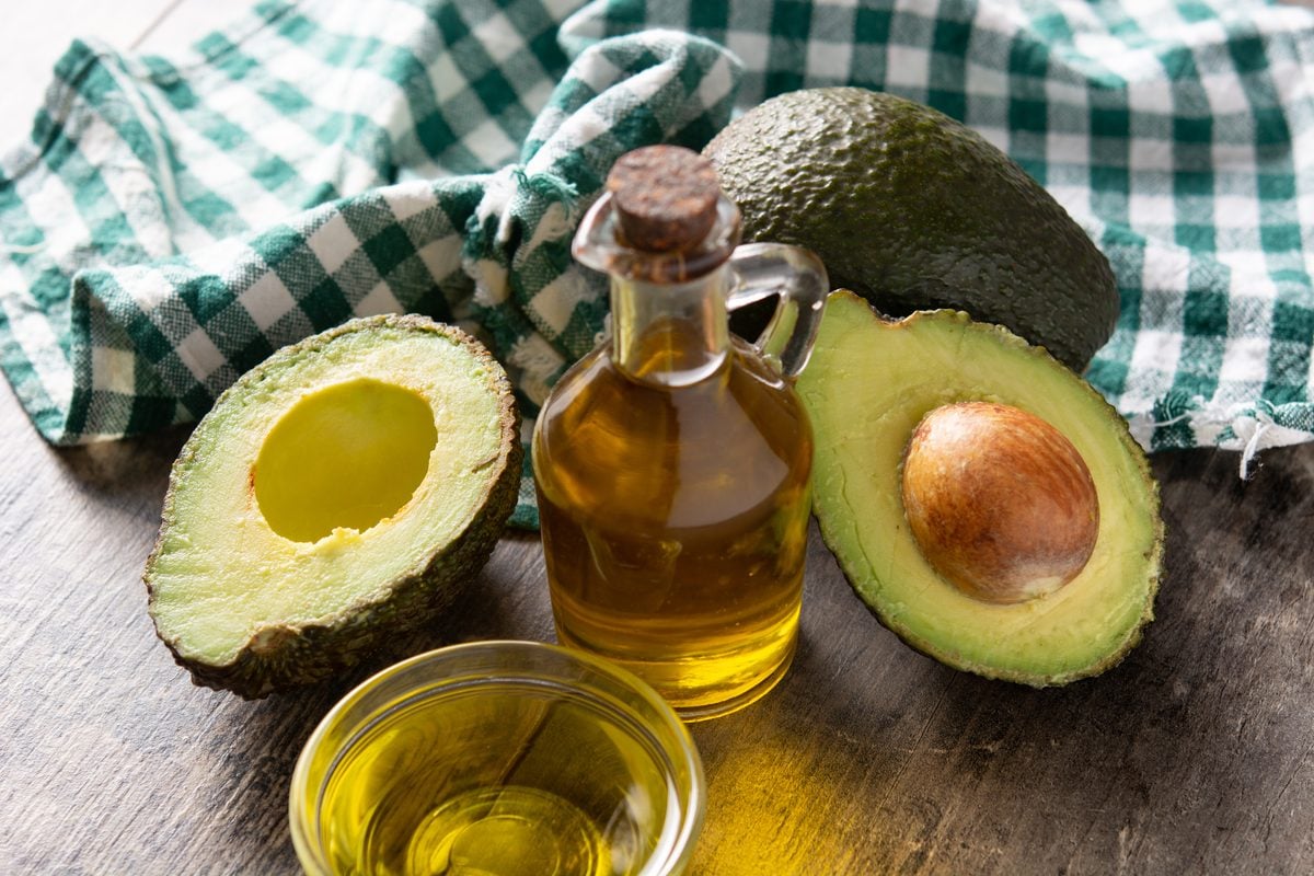 Halbierte Avocados neben einer Karaffe und einer Schale mit Olivenöl auf Holz
