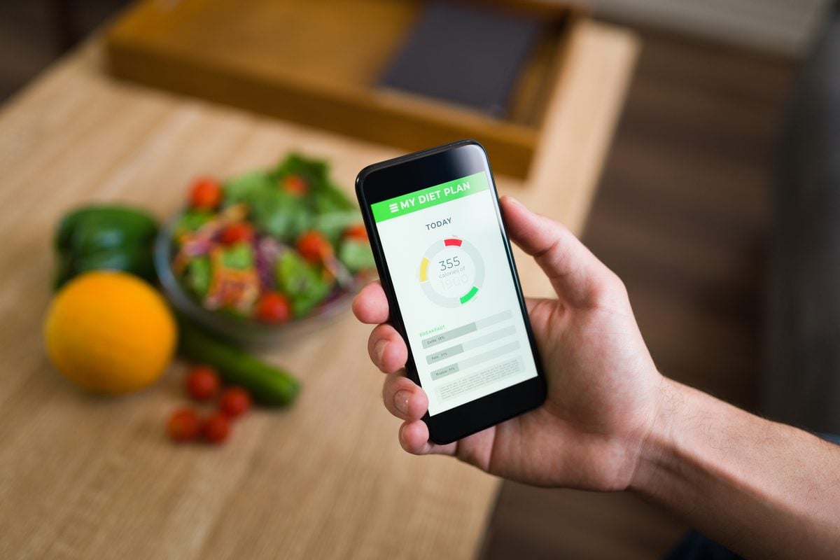 Hand hält ein Smartphone mit einer Kalorien-App, im Hintergrund eine Salatschale