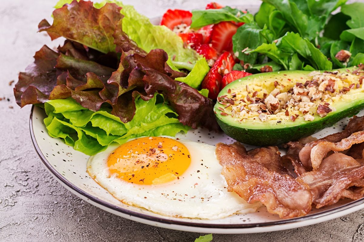 Keto für Anfänger: In 5 Schritten in die Ketose 1 Teller mit Spiegelei, Bacon, gefüllter Avocadohälfte, Salat und Erdbeeren