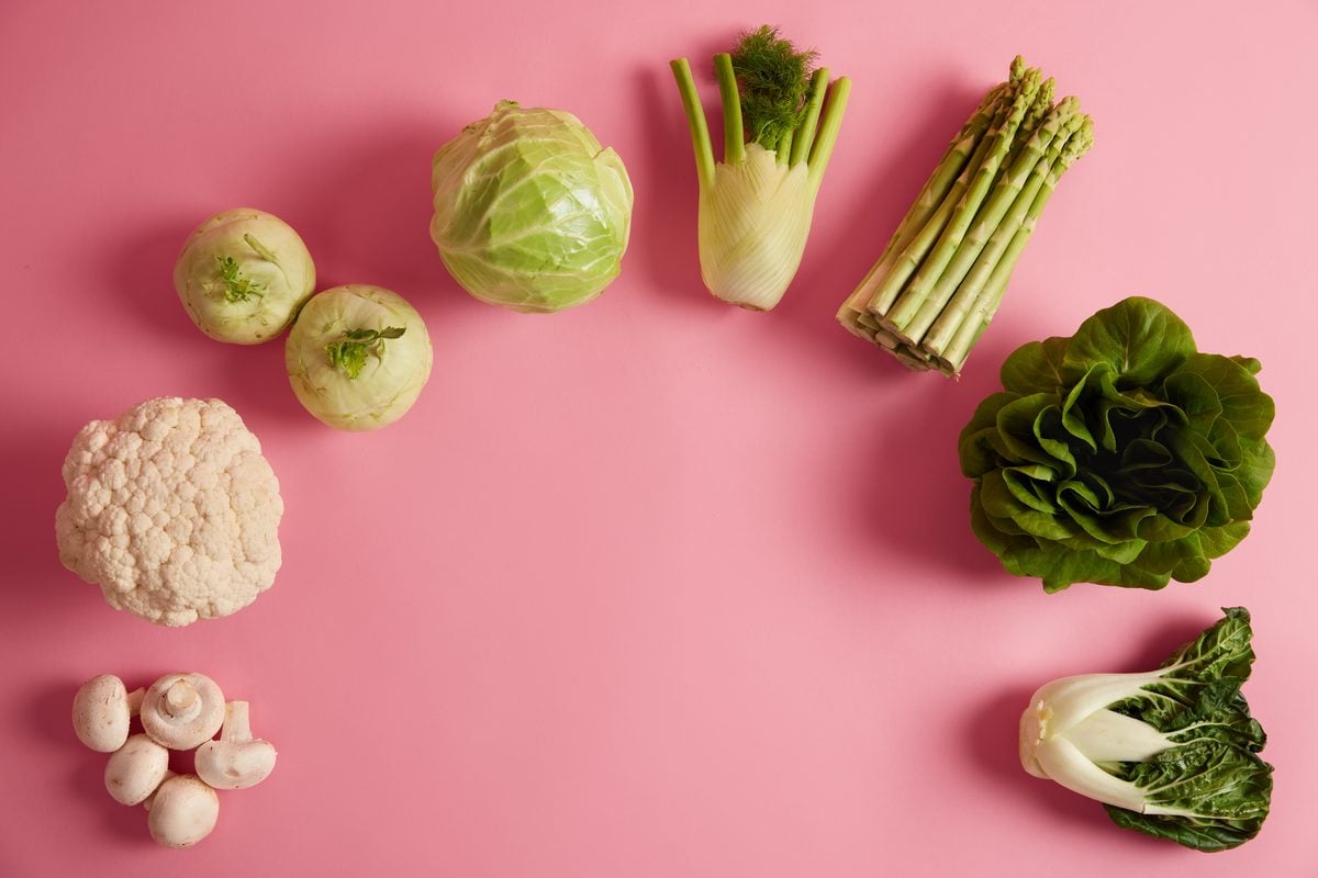 Blumenkohl, Rosenkohl, Weißkohl, Fenchel, grüner Spargel, Salat, Pak Choi und Champignons im Halbkreis auf rosa Hintergrund