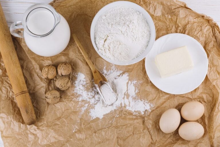 Schale mit Mehl, Butter, Eier, Walnüsse, ein Krug Milch und ein Nudelholz auf Backpapier