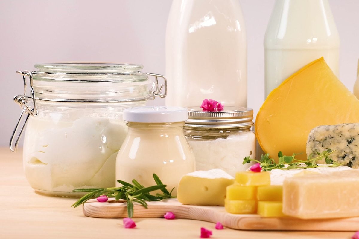 Hartkäse, Blauschimmelkäse, Butter, Frischkäse im Bügelglas und Milchflaschen auf einem Holzbrett