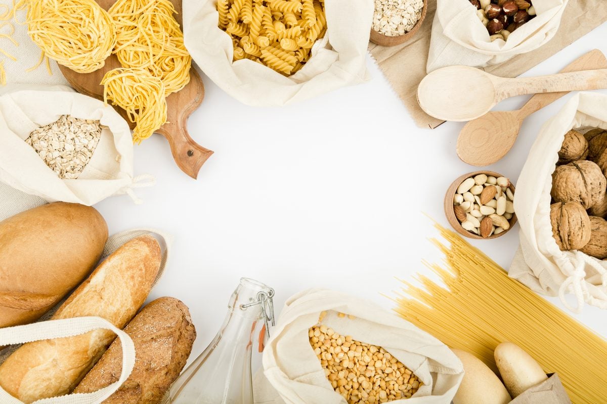 Wie viele Kohlenhydrate bei Keto? Das Netto-Limit pro Tag 1 Brot, Nudeln, Haferflocken, Linsen und Nüsse in Stoffbeuteln rund um eine leere Fläche